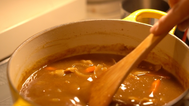 煮込んだカレーの鍋をかき混ぜる様子。