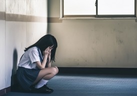部屋の隅でしゃがみ込む女子高生の姿