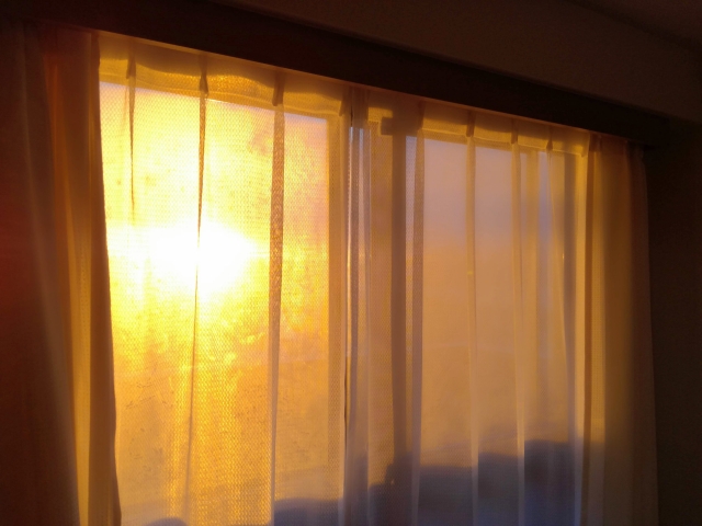 カーテン越しの窓辺に夕日が射す様子